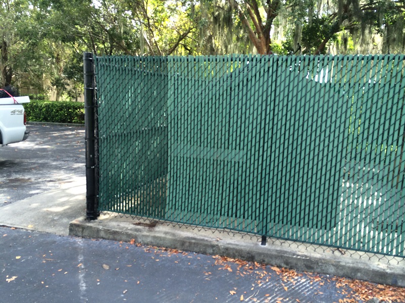 Commercial dumpster enclosure chain link fence repaired with green privacy slats in Orlando, FL.